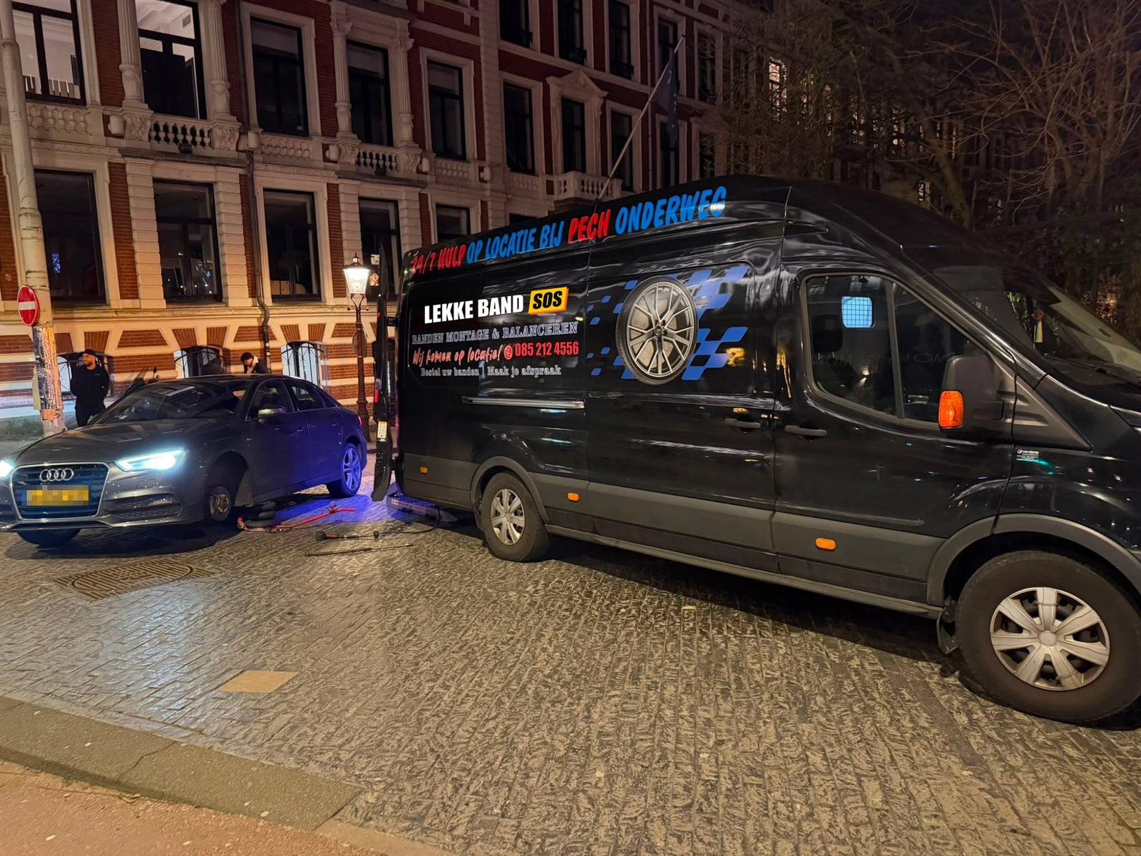 Lekke band auto: 's avonds een lekke autoband vervangen bij een Audi, met de bus van Lekke Band SOS erachter
